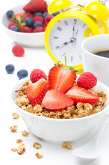 Granola with fresh berries, coffee, yellow alarm clock isolated