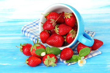 Ripe sweet strawberries in cup on blue wooden table