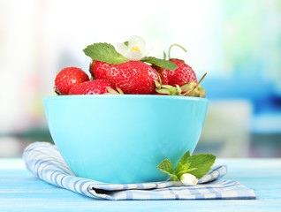 Ripe sweet strawberries in bowl on blue wooden table