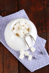 Refined sugar in white sugar bowl on wooden background