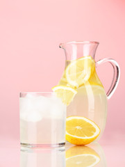 Lemonade in pitcher and glass on red background