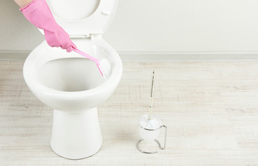 Woman hand with brush cleaning a toilet bowl in a bathroom