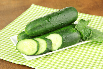 Tasty green cucumbers on color napkin, on wooden background