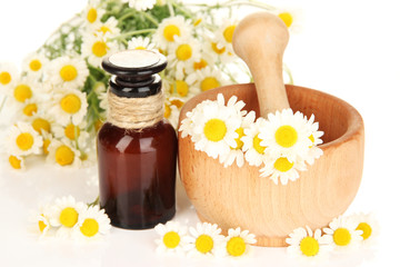Essential oil and chamomile flowers in mortar close up