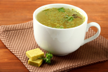 Cup of soup with bouillon cubes on wooden background