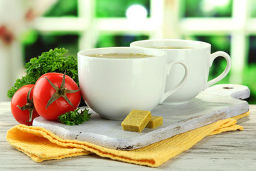 Cups of soup with bouillon cubes on wooden table