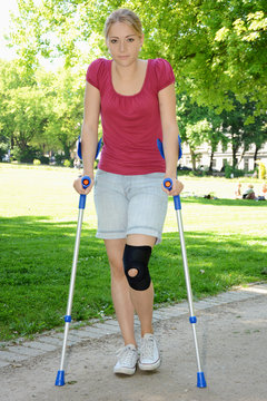 Junge Frau mit Kniebandage geht an Krücken