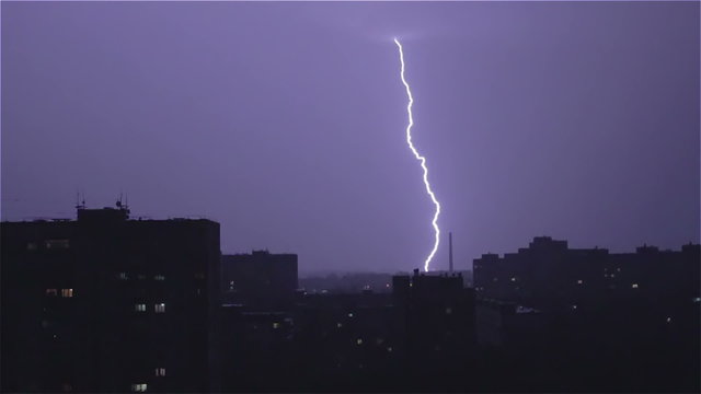 Large wide lightning bolt strikes night city, rain and thunder