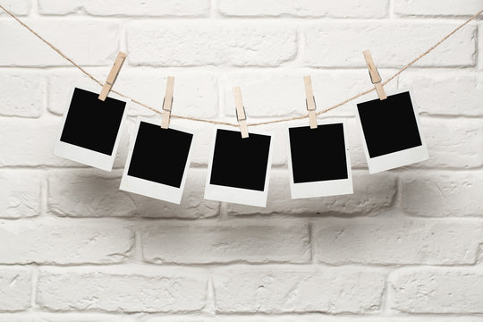 Blank photos hanging on a clothesline over brick wall background