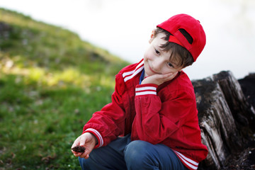 Cute child sitting at river in red cap