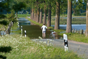 Mann mit Fahrrad/ Fahrradfahrer steht auf überschwemmter/ überfluteter Straße bei Hochwasser,...
