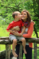 Fototapeta na wymiar Young handsome boy kissing mom's cheek on bridge