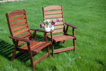 two wood chairs on the grass with vase of flowers on them