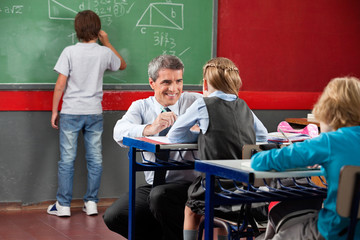 Teacher Looking At Schoolgirl While Crouching At Desk