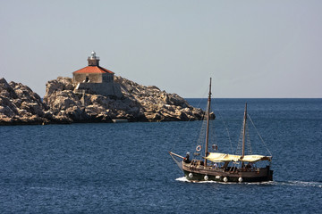 Naklejka premium Lighthouse on the rock near Dubrovnik and old wooden boat
