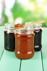 Tasty jam in banks on table on bright background