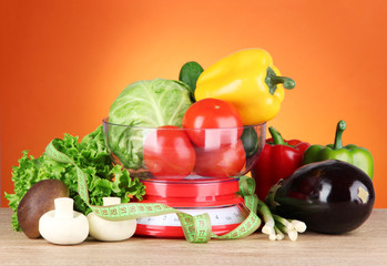 Fresh vegetables in scales on table on orange background