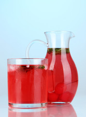 Cherry drink in pitcher and glass on blue background.