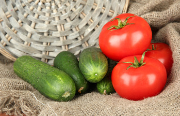 Tasty green cucumbers and red tomatoes on sackcloth background