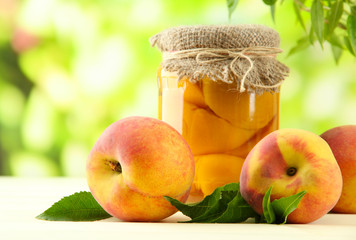 Jar of canned peaches and fresh peaches on wooden table,