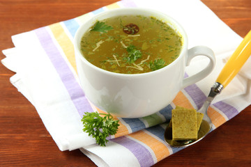 Cup of soup with bouillon cubes on wooden background
