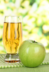 Glass of fresh apple juice on table on bright background
