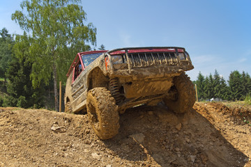 Red SUV overcomes steep muddy slope.