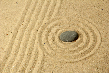 Fototapeta na wymiar Zen garden with raked sand and round stone close up