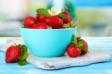 Ripe sweet strawberries in bowl on blue wooden table