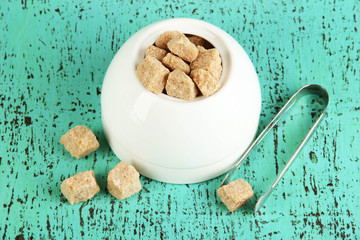 Unrefined sugar in white sugar bowl on wooden background
