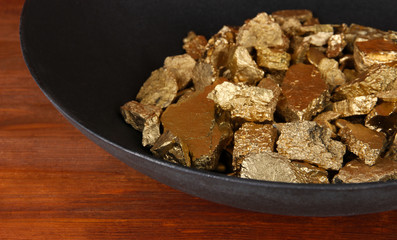 Gold pan with golden nuggets inside on wooden background