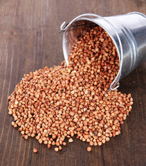Overturned bucket with grains on wooden background
