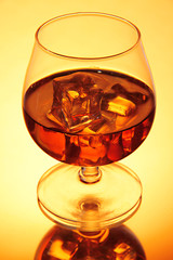 Brandy glass with ice on yellow background
