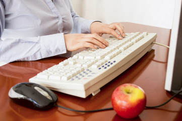 Human hands working on a computer keyboard  one apple to eat