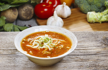Bowl of tomato soup and fresh vegetables on old wooden table