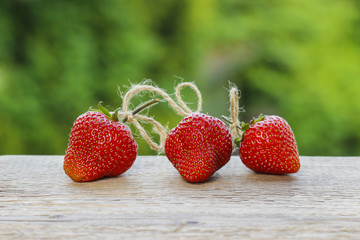 Three raw ripe strawberries on wooden table in lush garden
