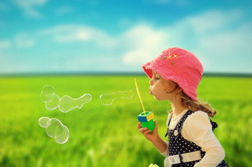 Little girl playing with soap bubbles outdoor in green field