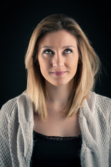 Fototapeta premium Doubtful blonde woman close up portrait on dark background.