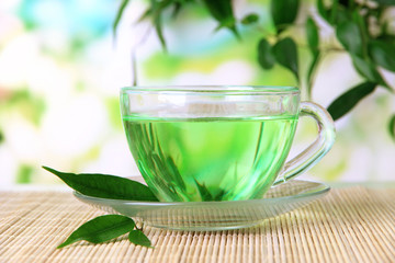 Transparent cup of green tea on bamboo mat, on nature