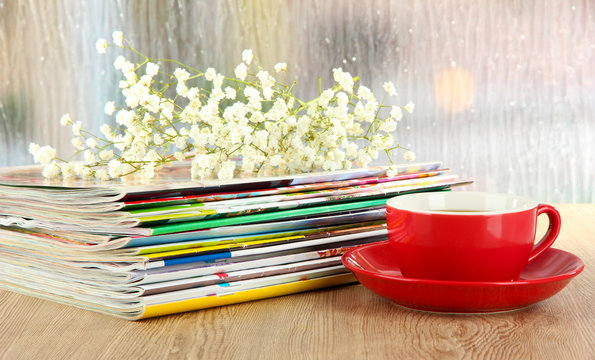 Many magazines with red cup on window background