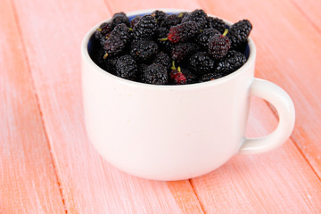 Ripe mulberries in cup on wooden background