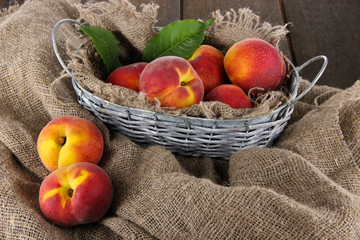 Fototapeta na wymiar Peaches in basket on sackcloth on wooden table