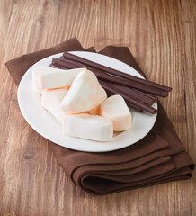 Marshmallows and chocolate sticks in plate on wooden table