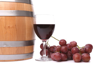 A glass of red wine with grapes and barrel.