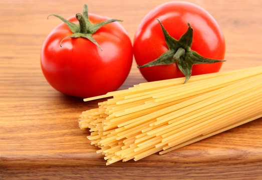 Tomatoesl and uncooked spaghetti on a cutting board