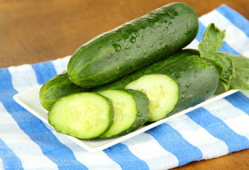 Tasty green cucumbers on color napkin, on wooden background