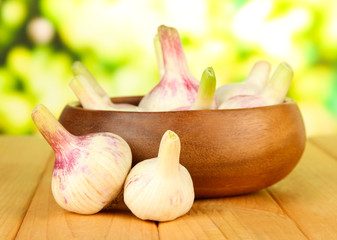 Fresh garlic in bowl, on wooden table, on bright background