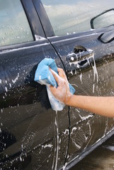 A Hand washing a black car with a sponge