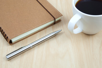 Cup of coffee on a wooden table with book and pen