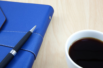 Cup of coffee on a wooden table with book and pen